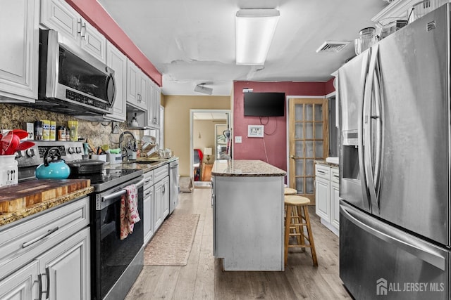 kitchen featuring stainless steel appliances, light wood finished floors, backsplash, and a sink