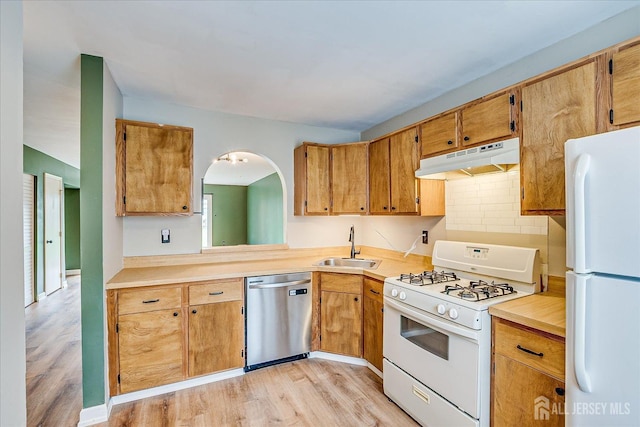 kitchen featuring light countertops, a sink, under cabinet range hood, and white appliances