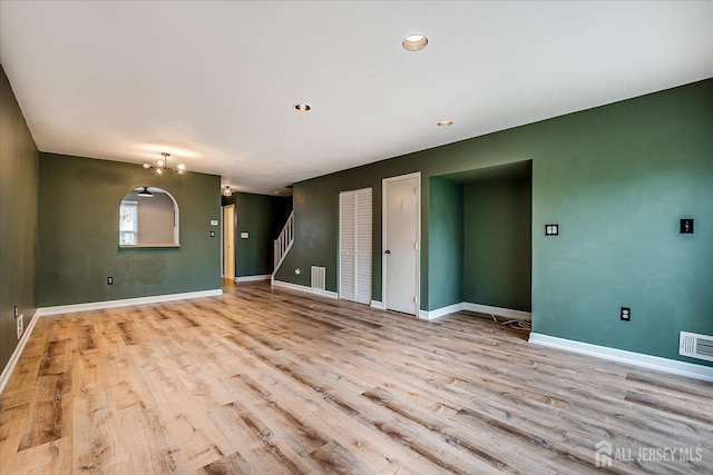 unfurnished living room with visible vents, baseboards, wood finished floors, a notable chandelier, and stairs