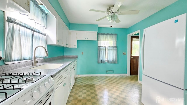 kitchen with white appliances, a sink, light floors, ceiling fan, and baseboards
