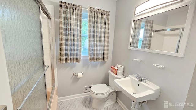 bathroom featuring toilet, a sink, bath / shower combo with glass door, and baseboards