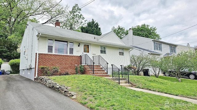 view of front of house with a chimney, brick siding, a front yard, and asphalt driveway