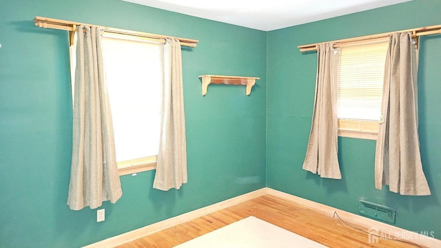 empty room with healthy amount of natural light, wood finished floors, and baseboards