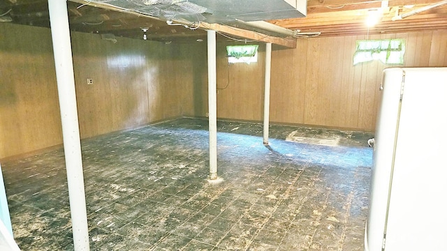 basement featuring white refrigerator, wood walls, and tile patterned floors