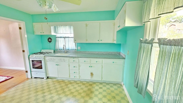 kitchen featuring white gas range, a sink, light floors, light countertops, and white cabinets