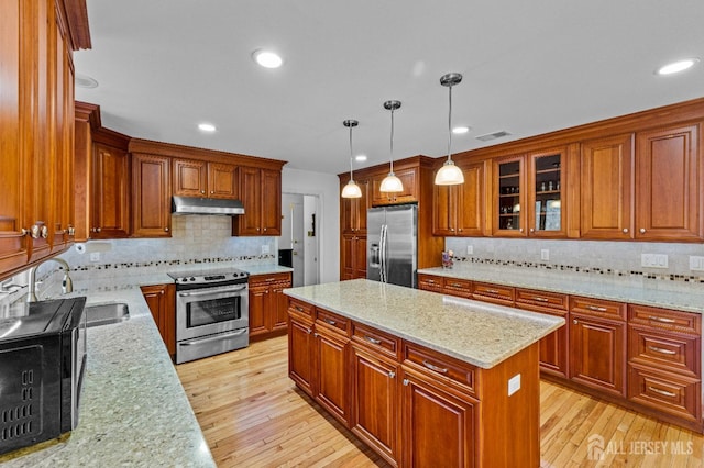 kitchen featuring sink, hanging light fixtures, a center island, stainless steel appliances, and light stone countertops