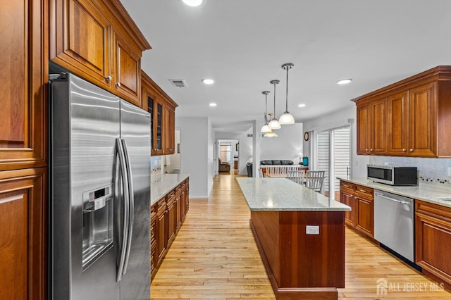 kitchen featuring stainless steel appliances, hanging light fixtures, light stone counters, and light hardwood / wood-style floors