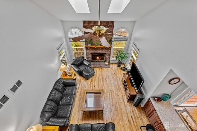 living room featuring plenty of natural light, a skylight, light hardwood / wood-style floors, and a brick fireplace