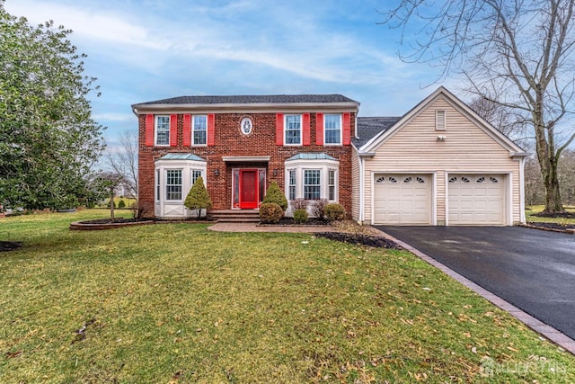 colonial-style house featuring a garage, a front yard, brick siding, and driveway