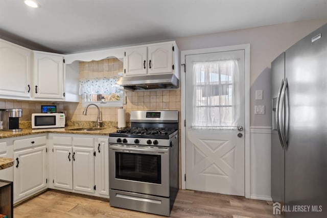 kitchen featuring sink, light hardwood / wood-style flooring, dark stone counters, stainless steel appliances, and white cabinets