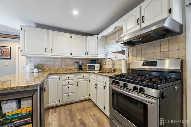 kitchen with stone countertops, sink, white cabinets, gas range, and light hardwood / wood-style flooring