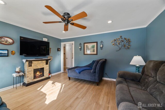 living room with ceiling fan, ornamental molding, a fireplace, and light hardwood / wood-style floors