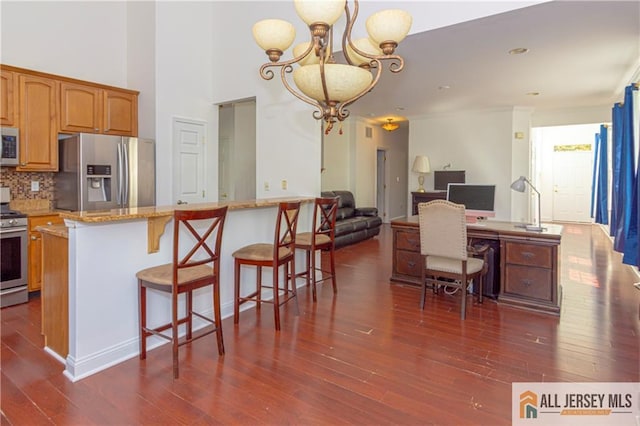 kitchen with hanging light fixtures, stainless steel appliances, an inviting chandelier, tasteful backsplash, and a kitchen bar