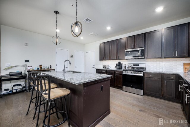 kitchen featuring a kitchen bar, a kitchen island with sink, sink, and appliances with stainless steel finishes