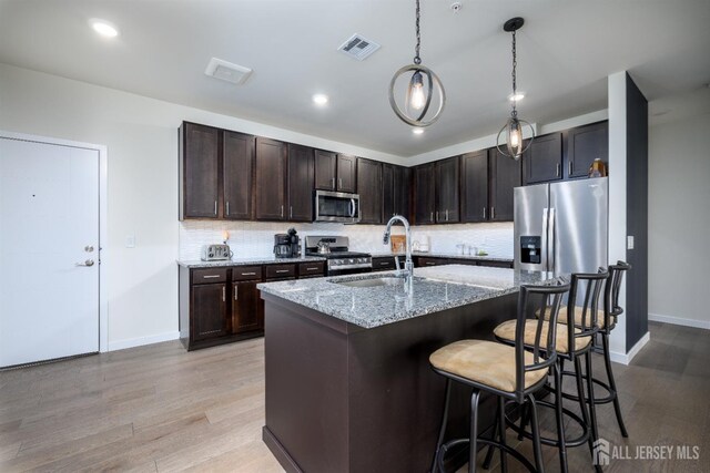 kitchen with a breakfast bar, sink, appliances with stainless steel finishes, light hardwood / wood-style floors, and light stone counters