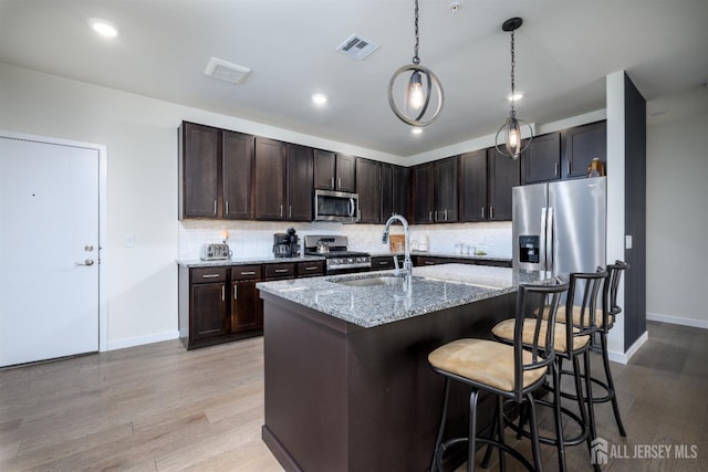 kitchen featuring a kitchen bar, sink, appliances with stainless steel finishes, light stone countertops, and decorative backsplash