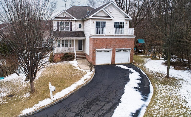 traditional-style home with aphalt driveway, a balcony, an attached garage, and brick siding