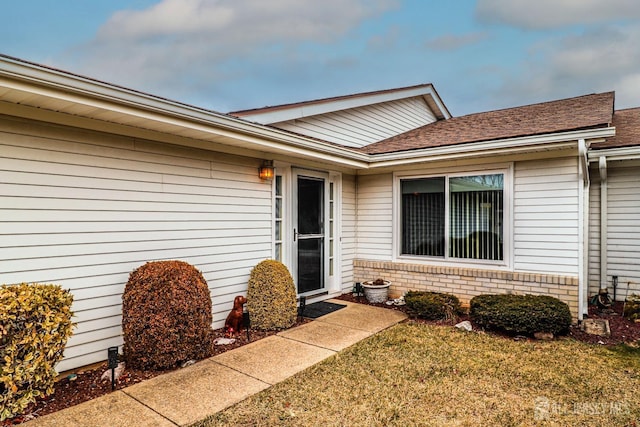 property entrance with a shingled roof, a lawn, and brick siding