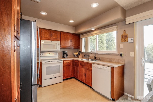 kitchen with a sink, white appliances, light countertops, and brown cabinets