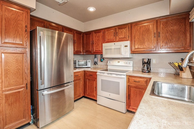 kitchen featuring brown cabinets, white appliances, light countertops, and a sink