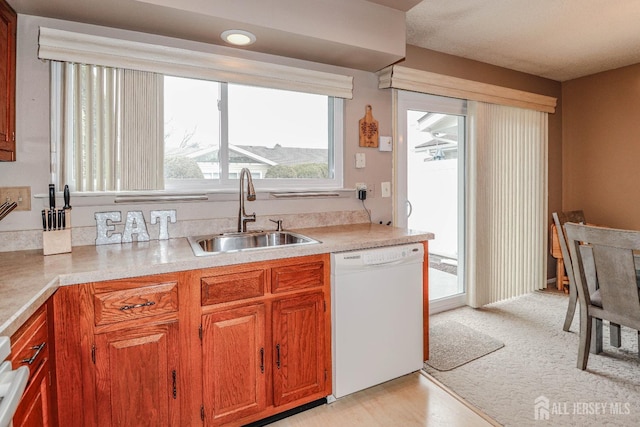 kitchen featuring light countertops, brown cabinetry, white dishwasher, and a sink