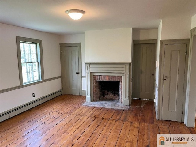 unfurnished living room featuring a brick fireplace, wood-type flooring, and a baseboard heating unit