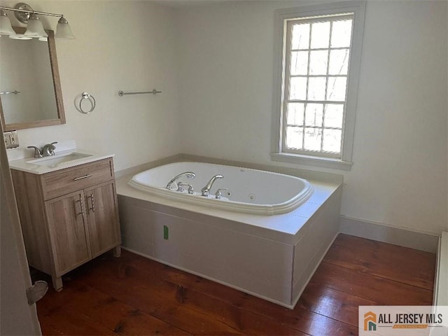 full bathroom with hardwood / wood-style flooring, baseboards, a tub with jets, and vanity