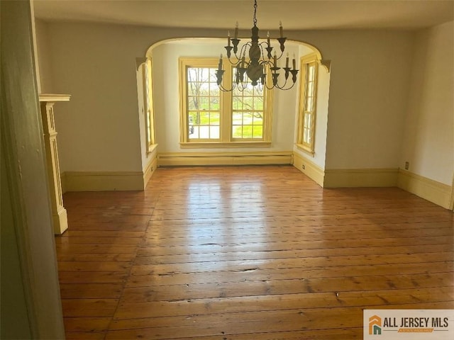 unfurnished dining area featuring arched walkways, a notable chandelier, baseboards, and hardwood / wood-style flooring