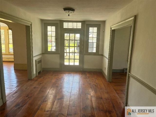 entryway with arched walkways, radiator, plenty of natural light, and hardwood / wood-style floors