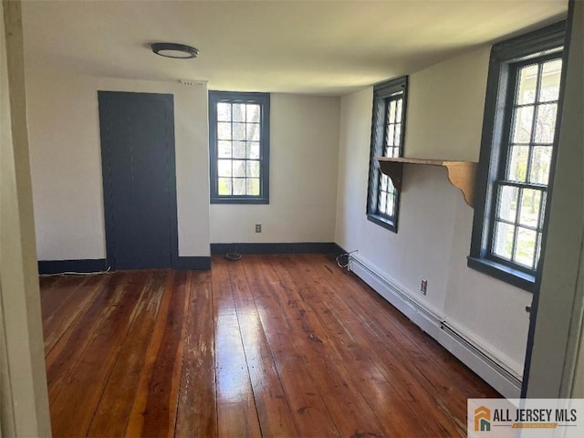 empty room with a baseboard radiator, wood-type flooring, plenty of natural light, and baseboards