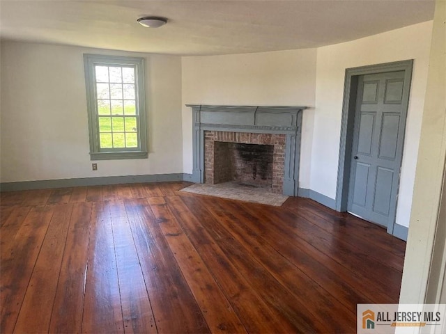 unfurnished living room featuring hardwood / wood-style floors, a brick fireplace, and baseboards