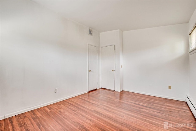 unfurnished room featuring light wood-style floors, a baseboard heating unit, and baseboards
