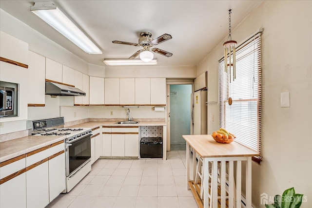 kitchen featuring gas range gas stove, a sink, under cabinet range hood, light countertops, and plenty of natural light