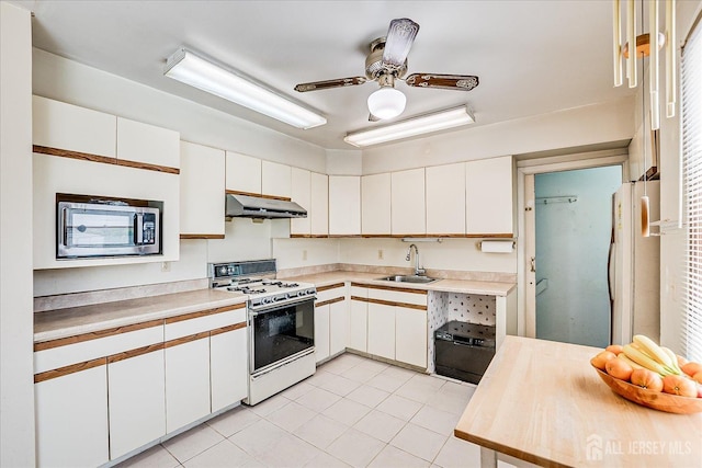 kitchen featuring white appliances, under cabinet range hood, a sink, light tile patterned floors, and light countertops