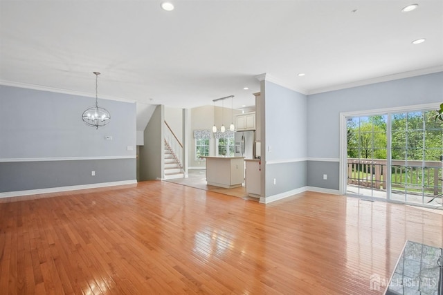 unfurnished living room featuring a chandelier, ornamental molding, baseboards, light wood-type flooring, and stairway