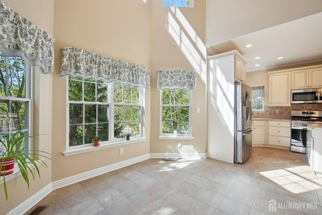 kitchen with stainless steel appliances, a towering ceiling, plenty of natural light, decorative backsplash, and baseboards