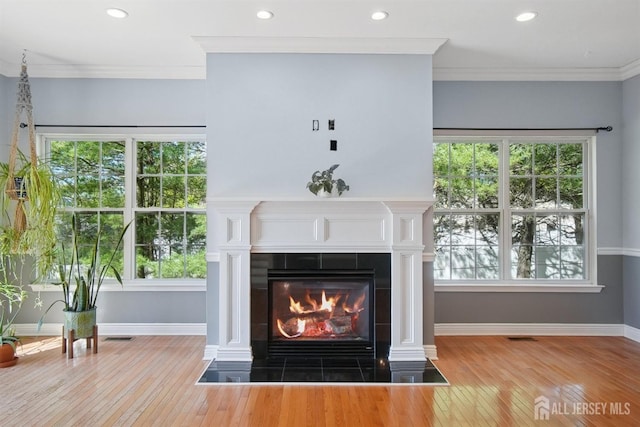 detailed view of wood finished floors, a tiled fireplace, baseboards, crown molding, and recessed lighting