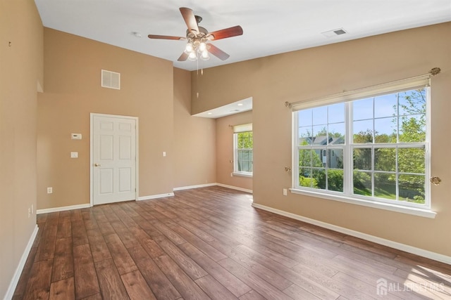 empty room with dark wood-type flooring, baseboards, ceiling fan, and a high ceiling