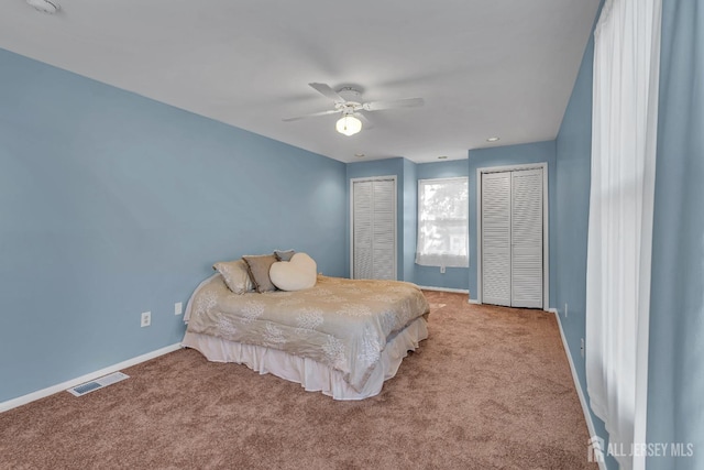 bedroom with baseboards, visible vents, carpet flooring, and two closets