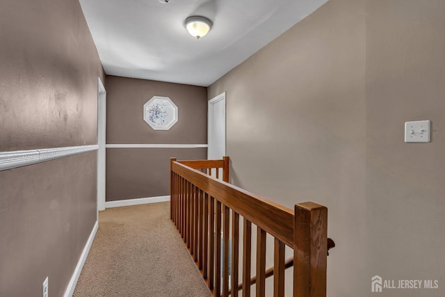 hallway featuring carpet floors, baseboards, and an upstairs landing