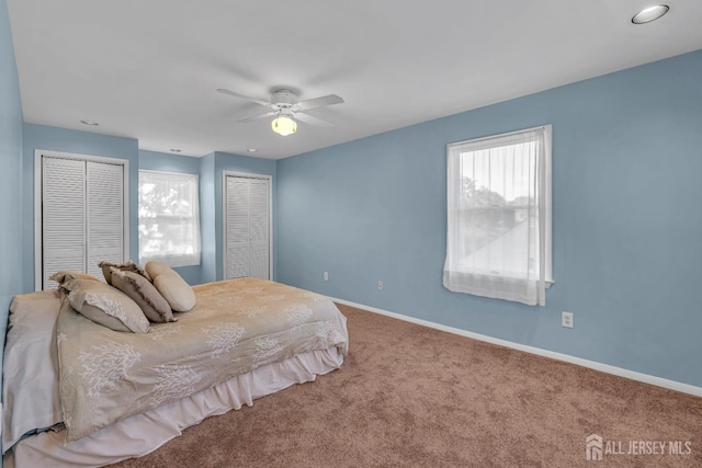 carpeted bedroom with multiple closets, a ceiling fan, and baseboards