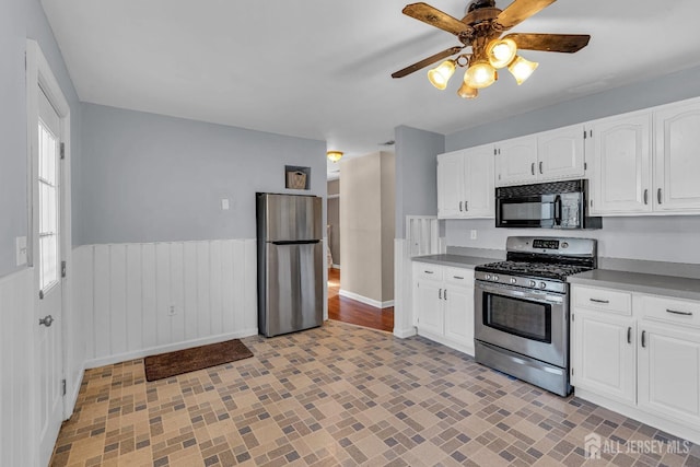 kitchen featuring baseboards, a ceiling fan, a wainscoted wall, stainless steel appliances, and white cabinetry