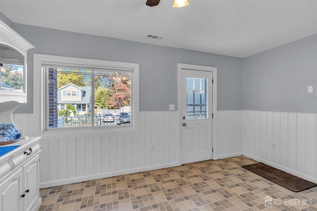 interior space with a ceiling fan, wainscoting, and visible vents