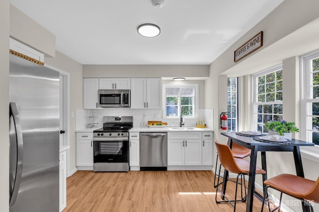 kitchen featuring light wood finished floors, a sink, stainless steel appliances, light countertops, and backsplash