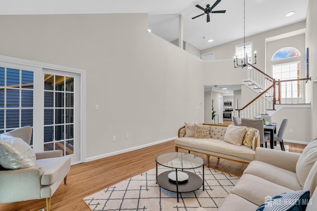 living room with stairway, baseboards, wood finished floors, and ceiling fan with notable chandelier