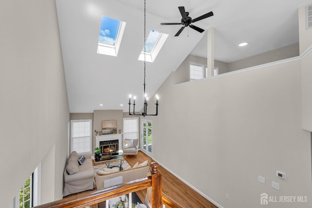 living area with a fireplace with flush hearth, high vaulted ceiling, wood finished floors, an inviting chandelier, and a skylight