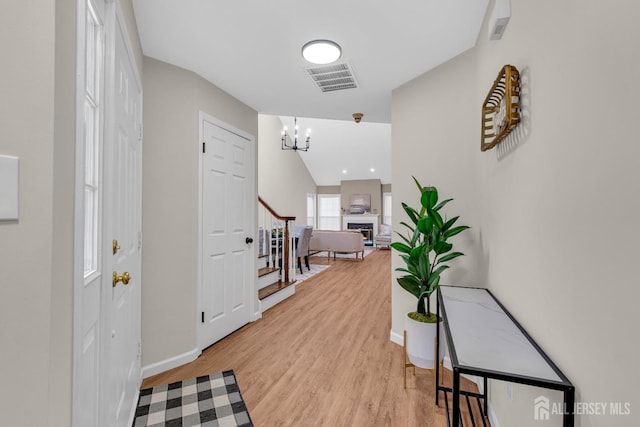 hallway featuring stairway, baseboards, visible vents, a notable chandelier, and light wood-type flooring