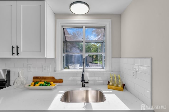 kitchen with a sink, backsplash, white cabinets, and light countertops