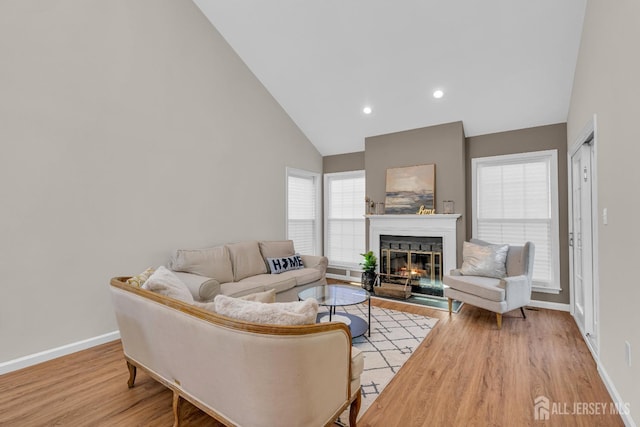 living area with baseboards, a lit fireplace, recessed lighting, light wood-style flooring, and high vaulted ceiling