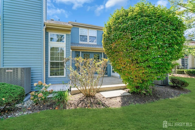 back of property featuring central AC unit, a shingled roof, and a yard